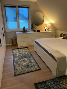 a bed room with a neatly made bed and two rugs on the wooden floor