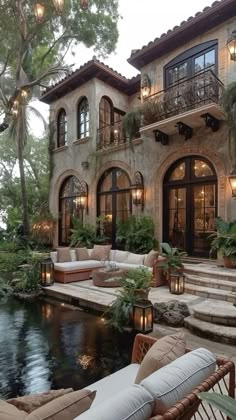 an outdoor living area with couches and tables next to a large pool in front of a house