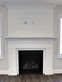 an empty living room with a fireplace and white walls, wood floors, and two windows