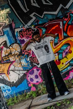 a man standing in front of a wall with graffiti on it's sides and arms behind his back