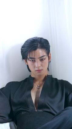 a young man sitting on top of a white chair next to a window with his shirt open