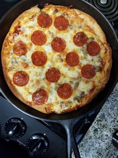 a pepperoni pizza sitting on top of a stove next to a frying pan