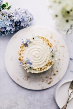 a white plate topped with a cupcake covered in frosting and blue hydrangeas