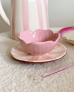 a pink cup and saucer sitting on top of a white rug next to a plate