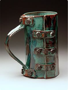 a green ceramic mug with metal rivets on it