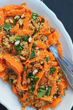 a white plate topped with carrots and nuts next to a silver fork on top of a wooden table