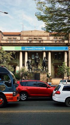 two cars are parked in front of a building with statues on the sides and columns