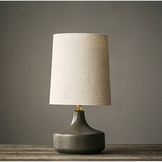 a gray table lamp on top of a wooden table next to a white and beige lampshade