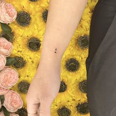 a person with a small tattoo on their left arm standing in front of sunflowers