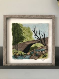 a watercolor painting of a bridge over a river with rocks and trees in the foreground