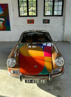 a colorful car parked in a garage next to two large windows and paintings on the wall