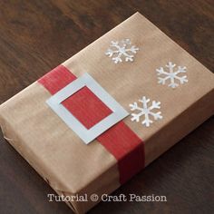 a gift wrapped in brown paper with red ribbon and snowflakes on the side