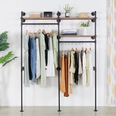 a rack with clothes hanging on it next to a potted plant