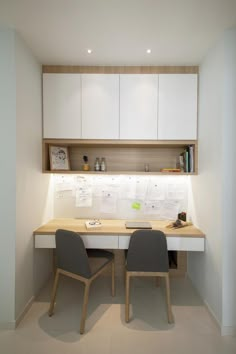 two chairs sitting at a desk in front of a white cabinet and shelves with papers on it