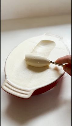 a person is holding a spoon over a plate with cream on it and there are two forks in the bowl