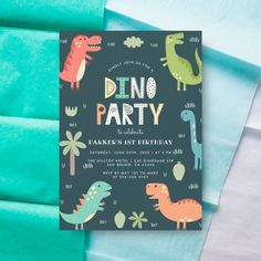 a dinosaur birthday party card on top of blue sheets with green and white paper in the background