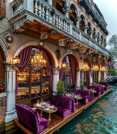 an outdoor restaurant with purple chairs and chandeliers next to the water's edge