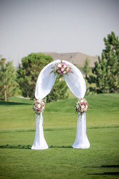 a wedding arch decorated with pink flowers and greenery on the golf course for an outdoor ceremony