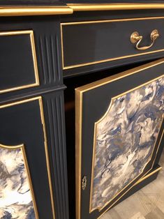 an ornate black and gold painted cabinet with marbled panels on the doors, drawers and handles