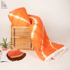 an orange and white blanket sitting on top of a bed next to a basket with a plant