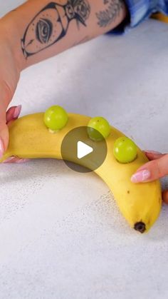 a person is holding a banana with green olives on it and pointing at the banana