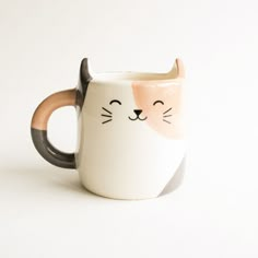 a ceramic mug with a cat's face painted on the front and sides, sitting on a white surface