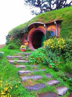 a green hobbot with steps leading up to it and flowers in the foreground