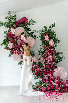 a woman in a white dress standing next to pink flowers and paper fan backdrops