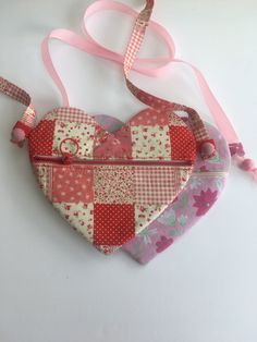 a patchwork heart shaped purse with pink ribbon hanging from it's side on a white surface