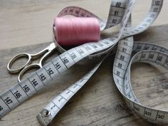 a pair of scissors, measuring tape and needle on a wooden table with pink thread