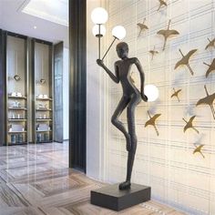 a statue is standing in front of a wall with birds on it and lights hanging from the ceiling