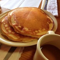 two pancakes on a plate with syrup and butter next to a cup of coffee or tea