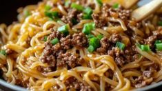 noodles with ground beef and green onions in a black bowl, ready to be eaten