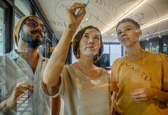 three people standing in front of a glass window with writing on it