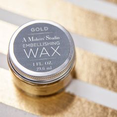 a jar of gold embellishing wax sitting on top of a striped table cloth