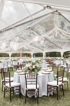 an outdoor tent with tables and chairs set up for a wedding reception in the grass