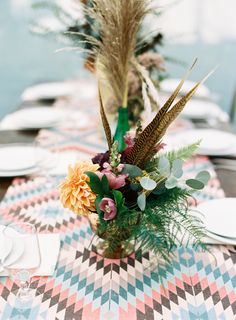 an arrangement of flowers and greenery sits on a table set for a formal dinner