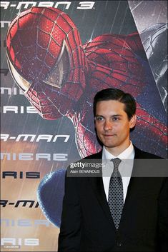 a man wearing a suit and tie standing in front of a spider - man poster