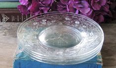 a glass bowl sitting on top of a blue book next to purple flowers and books