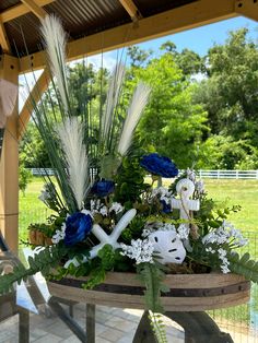 an arrangement of flowers and plants in a basket on a table outside with a fence behind it