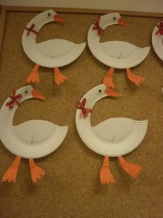 four paper plates shaped like ducks with red bows on their heads and legs, sitting on a cork board