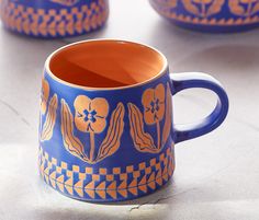 two blue and orange mugs sitting on top of a white table next to each other