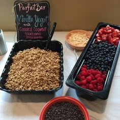 two trays filled with granola, raspberries and blueberries on a table