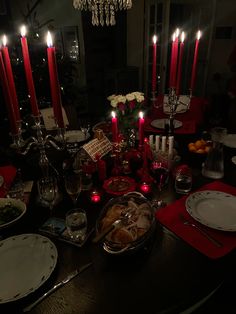 a dining room table is set with red candles and plates, silverware, and wine glasses