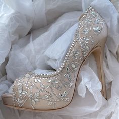 a pair of high heeled shoes with beading and pearls on the heels are sitting on some white fabric