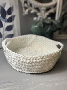 a white crocheted basket sitting on top of a table next to a mirror