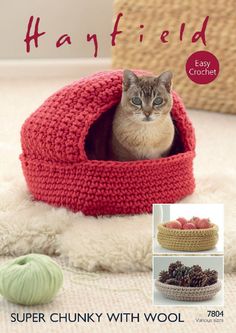 a cat is sitting in a crocheted bed with balls of yarn around it