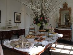 a table filled with desserts on top of a white cloth covered table next to a mirror