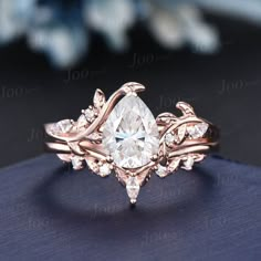 a ring with a pear shaped diamond surrounded by leaves and diamonds on the sides, sitting on top of a blue surface