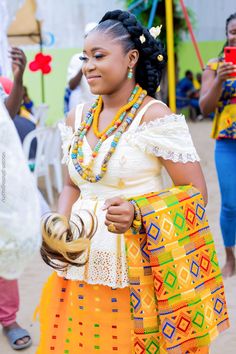 a woman in an orange and yellow dress is holding a gold object while standing next to other people